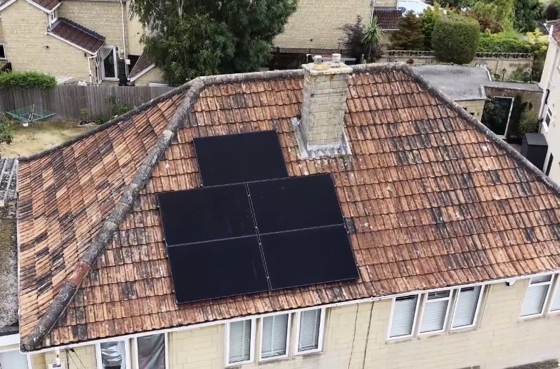 All-black solar panels installed by Cube Solar on a traditional clay-tiled roof beside a stone chimney
