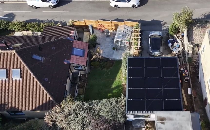 Drone view of a Bath house and garden with fifteen all-black solar panels on the flat garage roof