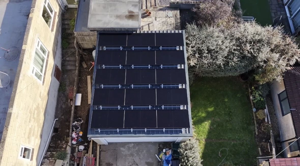 Top-down drone view of five rows of all-black LONGi solar panels on a tilted K2 mounting system on a flat metal garage roof